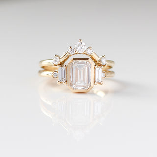 Yellow gold ring with a bezel set white emerald cut diamond and four white diamond accents with a yellow gold wedding band with round white diamonds, front view