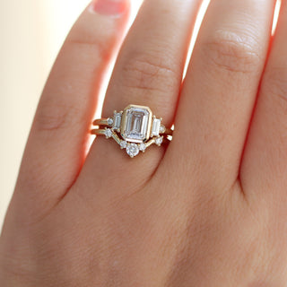 Yellow gold ring with a bezel set white emerald cut diamond and four white diamond accents with a yellow gold wedding band with round white diamonds, on hand