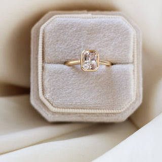 Yellow gold solitaire engagement ring with a bezel set peach radiant cut sapphire, in ring box, top view