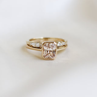 Yellow gold solitaire engagement ring with a bezel set peach radiant cut sapphire stacked with a white diamond straight wedding band, front view