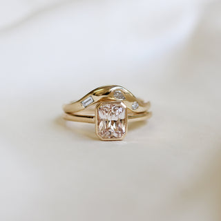 Yellow gold solitaire engagement ring with a bezel set peach radiant cut sapphire stacked with a white diamond curved wedding band, front view