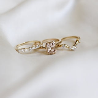 Yellow gold solitaire engagement ring with a bezel set peach radiant cut sapphire side by side with a white diamond straight wedding band and a white diamond curved wedding band, front view