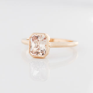Yellow gold solitaire engagement ring with a bezel set peach radiant cut sapphire, quarter view