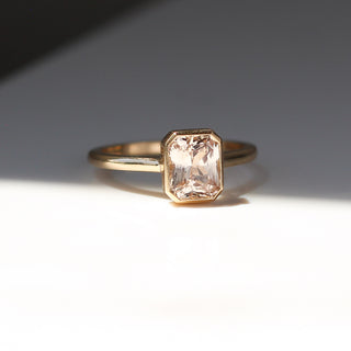 Yellow gold solitaire engagement ring with a bezel set peach radiant cut sapphire, quarter view