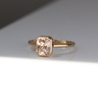 Yellow gold solitaire engagement ring with a bezel set peach radiant cut sapphire, quarter view