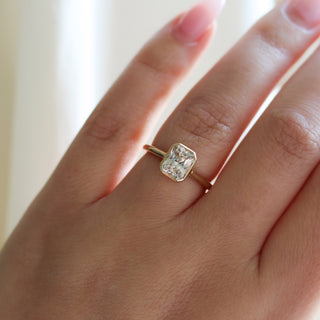 Yellow gold solitaire engagement ring with a bezel set peach radiant cut sapphire, on hand, top view