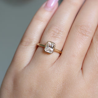 Yellow gold solitaire engagement ring with a bezel set peach radiant cut sapphire, on hand, top view