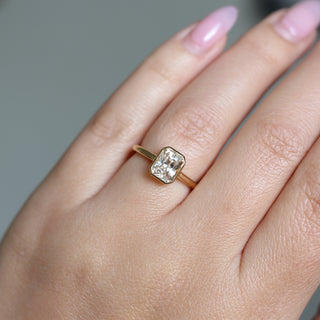 Yellow gold solitaire engagement ring with a bezel set peach radiant cut sapphire, on hand, top view