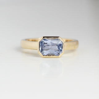 Yellow gold solitaire engagement ring with a bezel set blue emerald cut sapphire