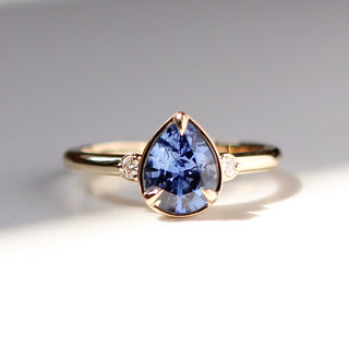 Yellow gold engagement ring with a pear blue sapphire and round diamond accents