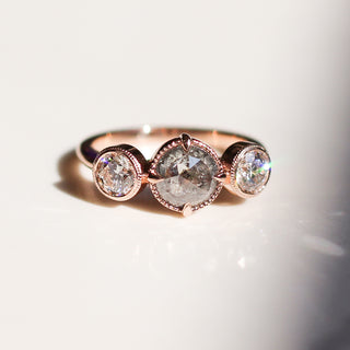 Three stone rose gold engagement ring with a salt and pepper round diamond and two white round diamonds