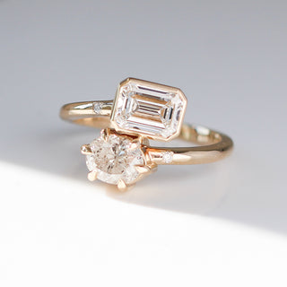 Yellow gold engagement ring with an bezel set emerald cut diamond and a prong set oval cut diamond in a toi et moi style