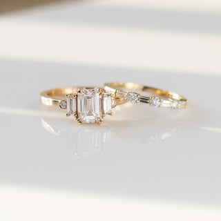 Yellow gold wedding band with baguette cut and round brilliant cut lab diamonds beside an emerald cut white diamond engagement ring, front view