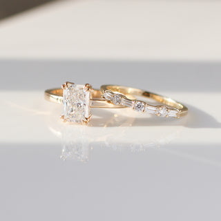 Yellow gold wedding band with baguette cut and round brilliant cut lab diamonds beside an emerald cut white diamond engagement ring, front view