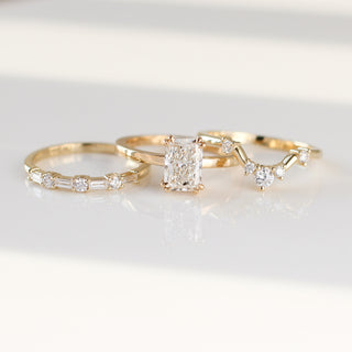 Yellow gold wedding band with baguette cut and round brilliant cut lab diamonds beside with an emerald cut white diamond engagement ring and a curved diamond wedding band, front view