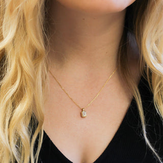 Gold necklace with a pendant worn by a person with blonde hair.