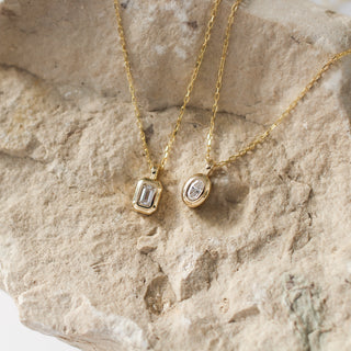 Two gold necklaces with pendants on a stone surface