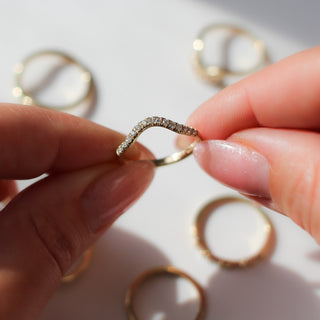 Diamond pave curved wedding band in yellow gold being held, with multiple yellow gold wedding bands in the background 