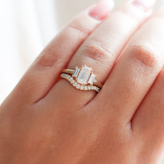 Diamond pave curved wedding band in yellow gold stacked with emerald cut diamond engagement ring, on hand