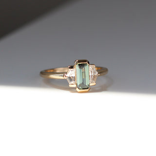 Three stone yellow gold ring, with elongated emerald cut green sapphire half bezel set and shield shaped white sapphire side stones in half bezel settings, quarter view