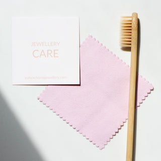 A jewellery cleaning kit with a pink polishing cloth, a recyclable bamboo brush, and a card reading 'JEWELLERY CARE'.