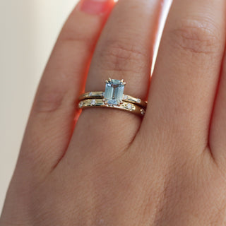 Yellow gold ring with a light blue emerald cut sapphire with yellow gold straight wedding band with white diamonds, on hand