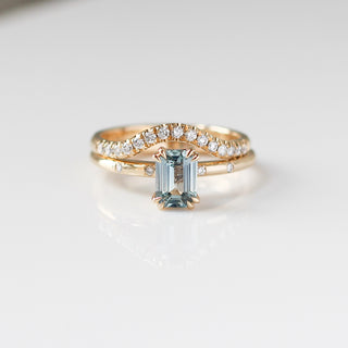 Yellow gold ring with a light blue emerald cut sapphire with yellow gold curved wedding band with white diamonds, front view