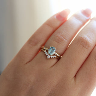 Yellow gold ring with a light blue emerald cut sapphire with yellow gold curved wedding band with white diamonds, on hand