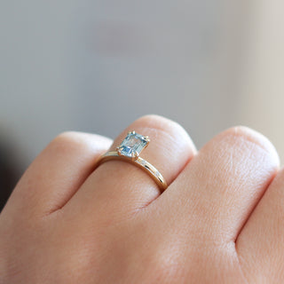 Yellow gold ring with a light blue emerald cut sapphire, on hand