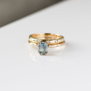 Yellow gold ring with a light blue emerald cut sapphire with yellow gold straight wedding band with white diamonds, front view