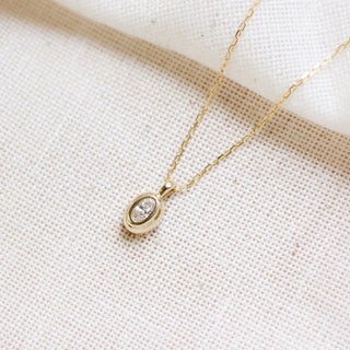 Gold necklace with a small pendant on a beige fabric background