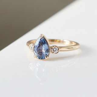 Three stone engagement ring with a blue pear cut sapphire in yellow gold, quarter view