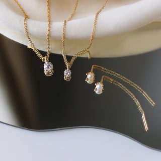 Pearl threader earrings in yellow gold and two round lab diamond necklaces in yellow gold side by side on mirror