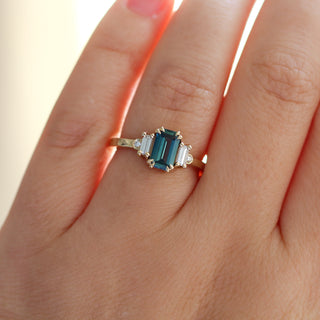 Yellow gold ring with a teal emerald cut sapphire and four white diamond accents, on hand