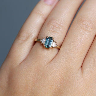 Yellow gold ring with a teal emerald cut sapphire and four white diamond accents, on hand