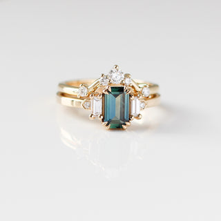 Yellow gold ring with a teal emerald cut sapphire and four white diamond accents and a yellow gold curved wedding band with round white diamonds, front view
