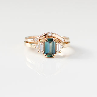 Yellow gold ring with a teal emerald cut sapphire and four white diamond accents and a yellow gold curved wedding band with round white diamonds, front view