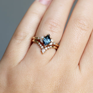 Yellow gold ring with a teal lozenge cut sapphire and white diamond accents with a yellow gold pointed wedding band with white diamonds, on hand