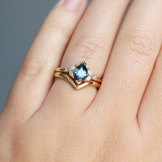 Yellow gold ring with a teal lozenge cut sapphire and white diamond accents with a yellow gold pointed wedding band, on hand