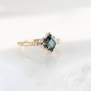 Yellow gold ring with a teal lozenge cut sapphire and white diamond accents, quarter view