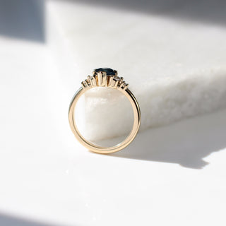 Yellow gold ring with a teal lozenge cut sapphire and white diamond accents, side view
