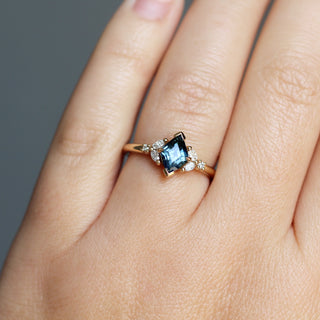 Yellow gold ring with a teal lozenge cut sapphire and white diamond accents, on hand