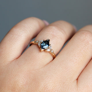 Yellow gold ring with a teal lozenge cut sapphire and white diamond accents, on hand