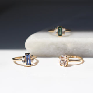 Three yellow gold engagement rings with coloured sapphires on a marble surface