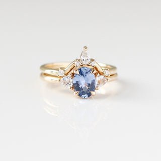 Yellow gold ring with a blue oval cut sapphire and two white trillion cut diamonds with a yellow gold curved wedding band with white diamonds, front view