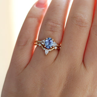 Yellow gold ring with a blue oval cut sapphire and two white trillion cut diamonds with a yellow gold curved wedding band with white diamonds, on hand