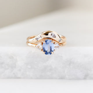 Yellow gold ring with a blue oval cut sapphire and two white trillion cut diamonds with a yellow gold curved wedding band with white diamonds, front view