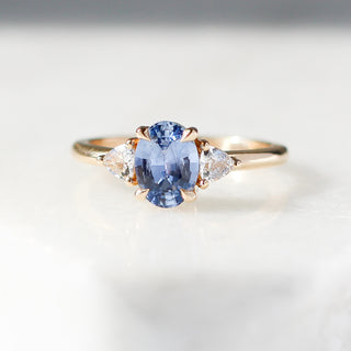 Yellow gold ring with a blue oval cut sapphire and two white trillion cut diamonds, front view