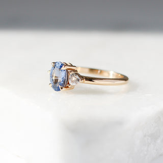 Yellow gold ring with a blue oval cut sapphire and two white trillion cut diamonds, quarter view