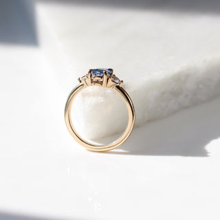 Yellow gold ring with a blue oval cut sapphire and two white trillion cut diamonds, side view